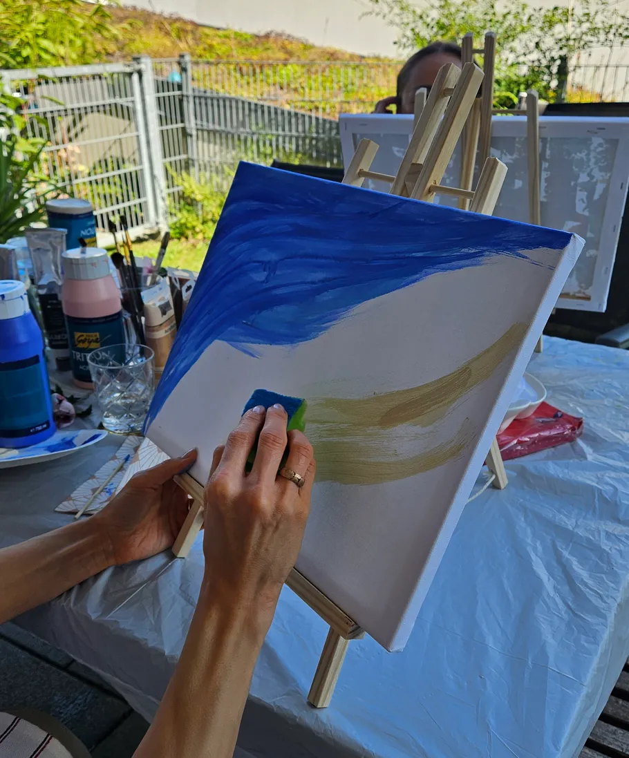 Person painting on canvas outdoors with sponge.