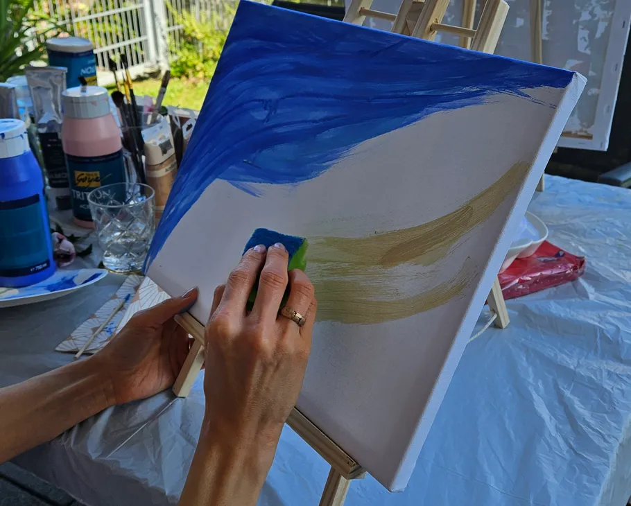 Person painting on canvas outdoors with sponge.