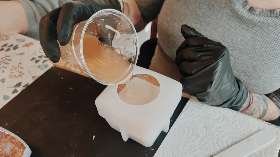 Person pouring liquid into mold, wearing gloves.
