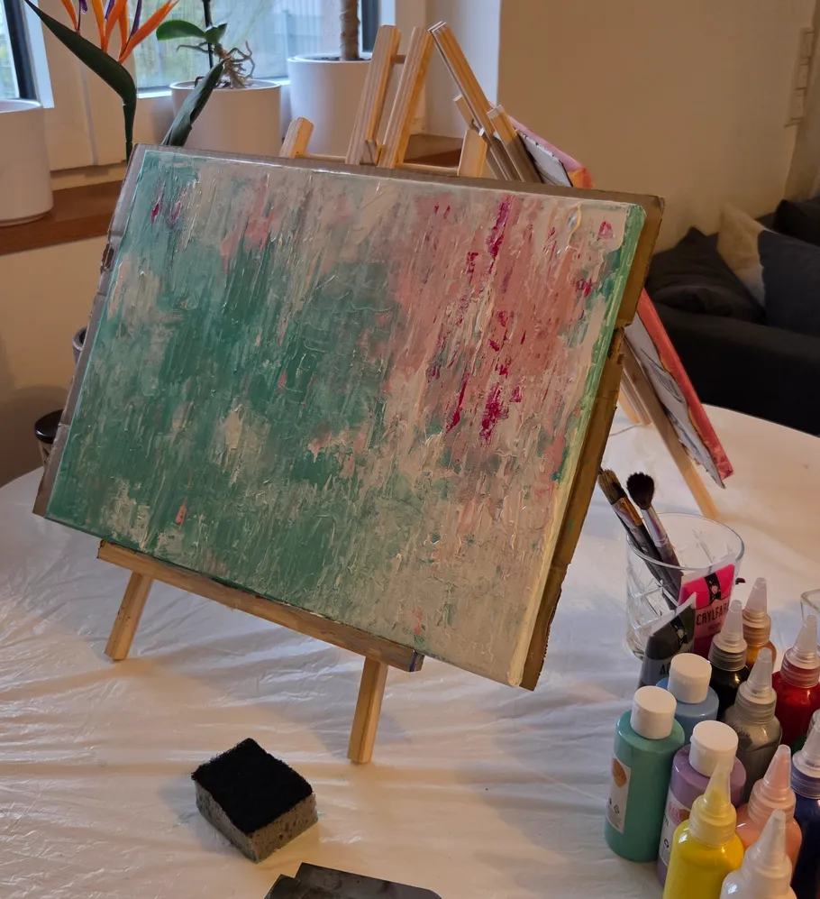 Abstract painting on easel with paint bottles.