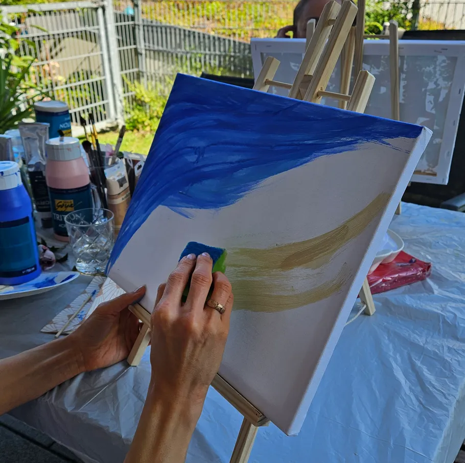Person painting on canvas with sponge outdoors.