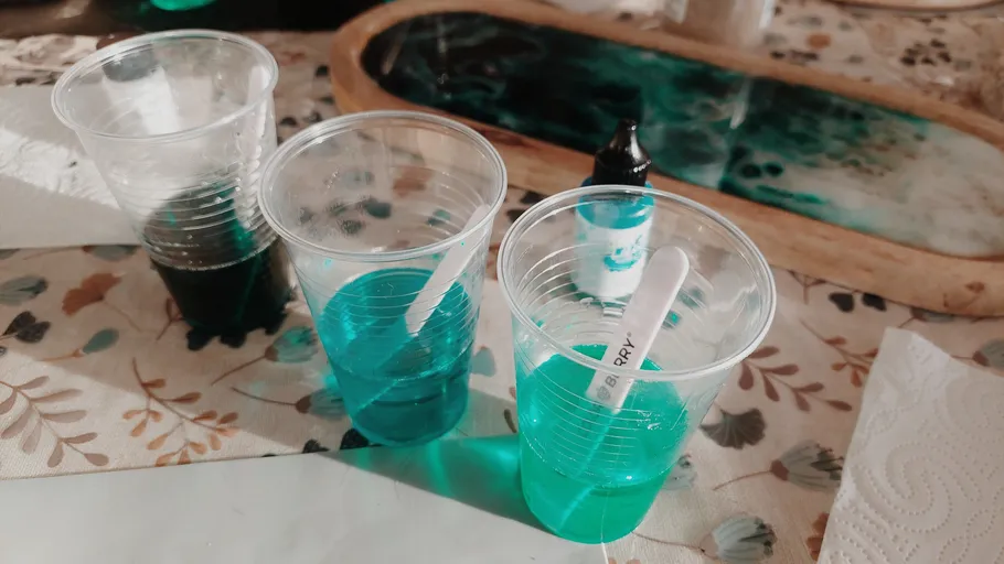 Plastikbecher mit grüner Flüssigkeit auf Blumen-Tischdecke.