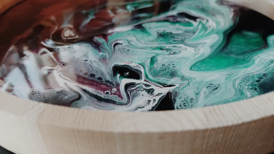 Colorful liquid swirls inside wooden bowl.