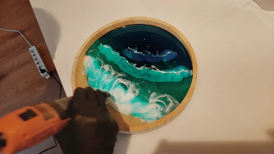 Person using tool on round epoxy artwork.