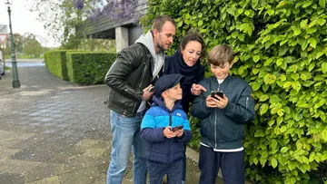 Familie schaut draußen auf Smartphone.