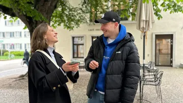Zwei Personen lächeln und sprechen im Freien.