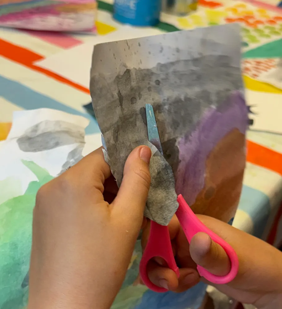 Kind schneidet bemaltes Papier mit rosa Schere.