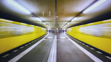 Gelber Zug fährt, gespiegelt im Bahnhof.