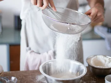 Flour is sifted through a sieve into a bowl.