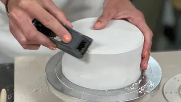 Person smoothing cake with a tool in kitchen.