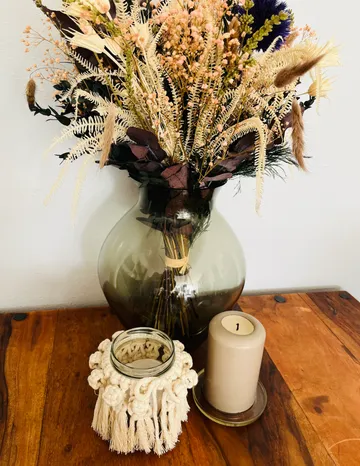 Getrocknete Blumen in Vase, Kerze auf Holztisch.