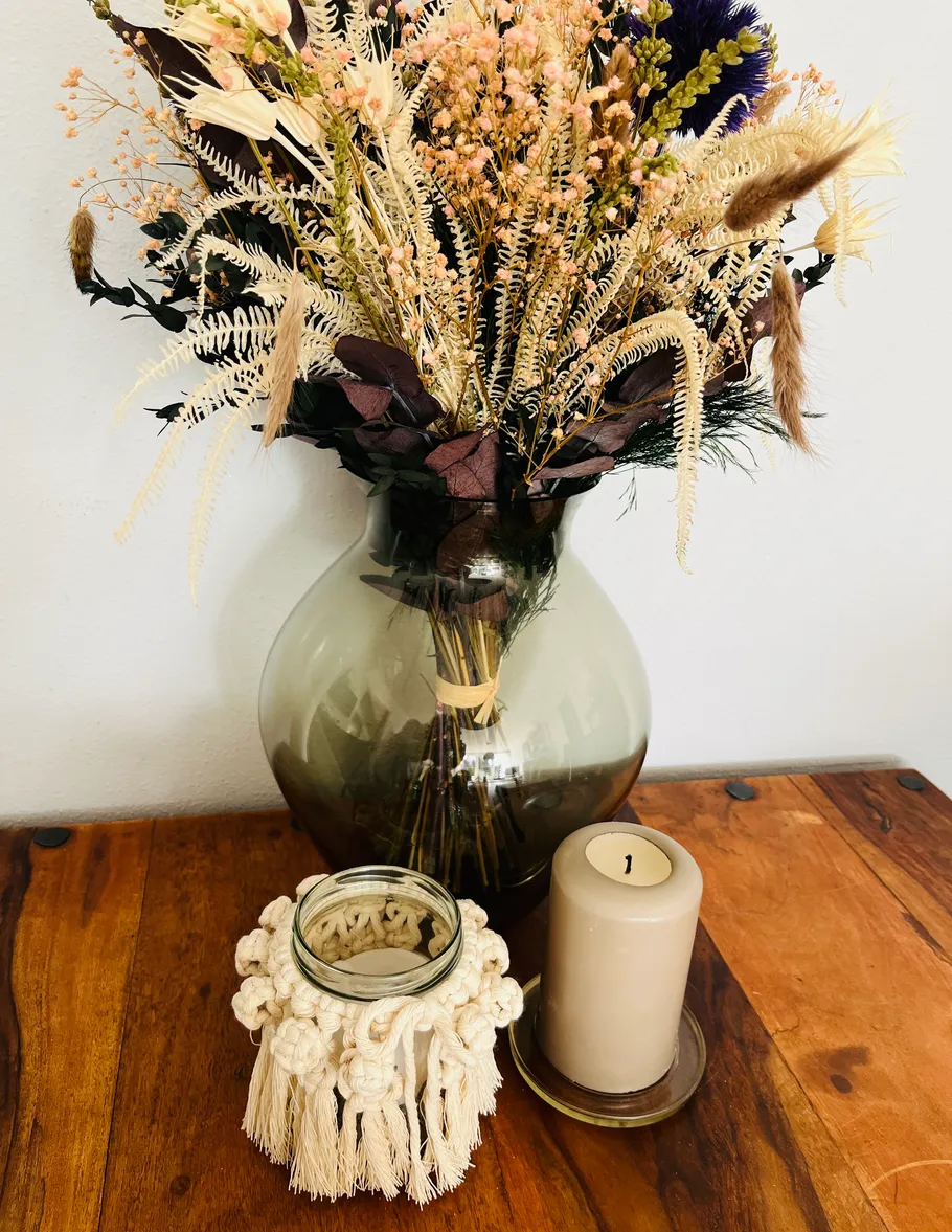 Getrocknete Blumen in Vase, Kerze auf Holztisch.