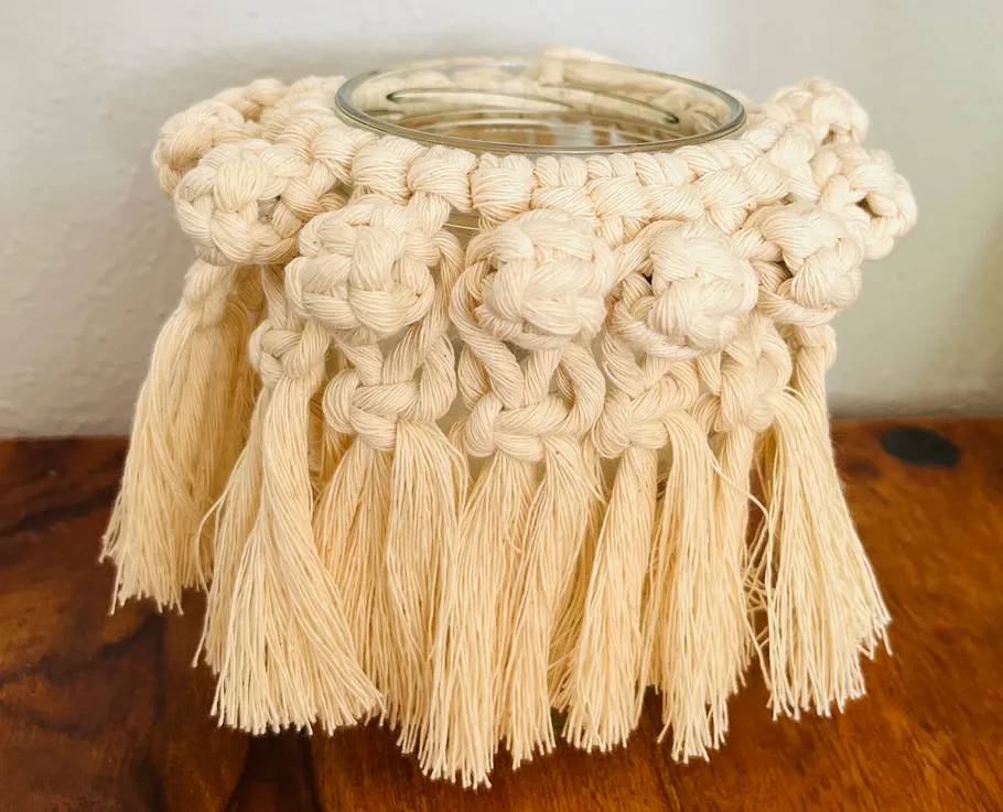 Macrame-covered jar with knotted design, wooden table.