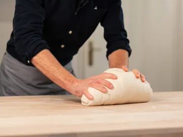 Dough is kneaded on a wooden surface.