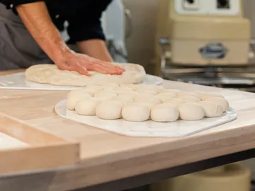 Teig wird bearbeitet, während Brötchen auf Tisch liegen.