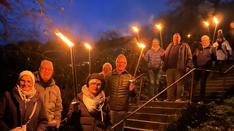 Personen halten Fackeln auf Treppe bei Nacht.