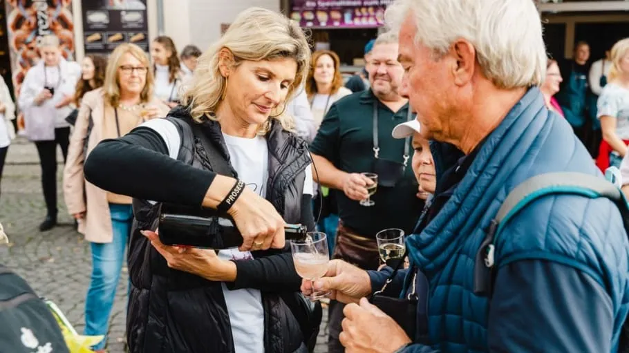 Frau schenkt einem Mann draußen Wein ein.