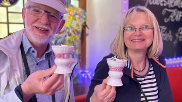 Two people smiling, holding ice cream cups indoors.