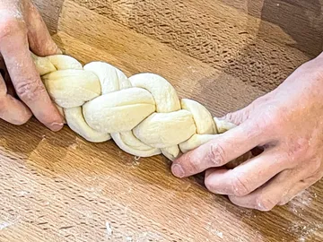 Teig wird zu einem geflochtenen Brot geformt. Holzoberfläche.