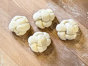 Four woven dough balls lie on a wooden table.