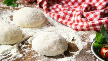 Pizzateigkugeln auf bemehlter Fläche mit Tuch.