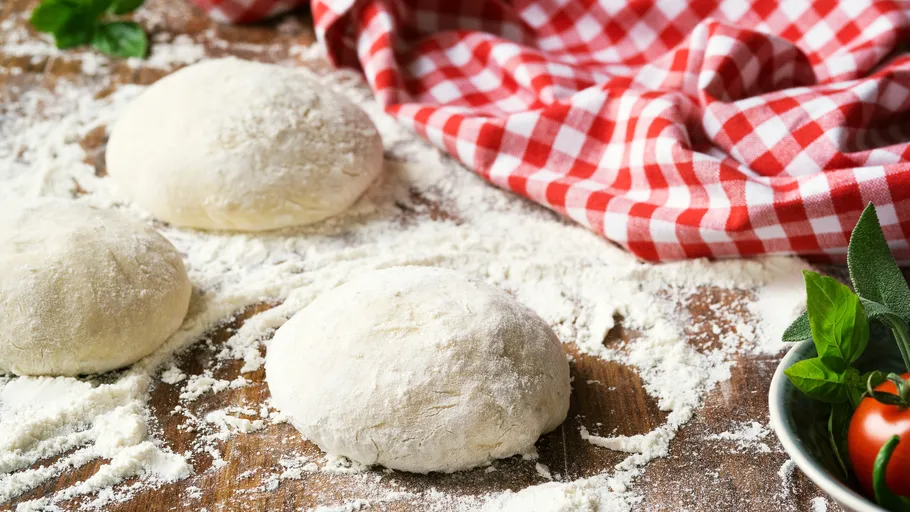 Pizzateigkugeln auf bemehlter Fläche mit Tuch.