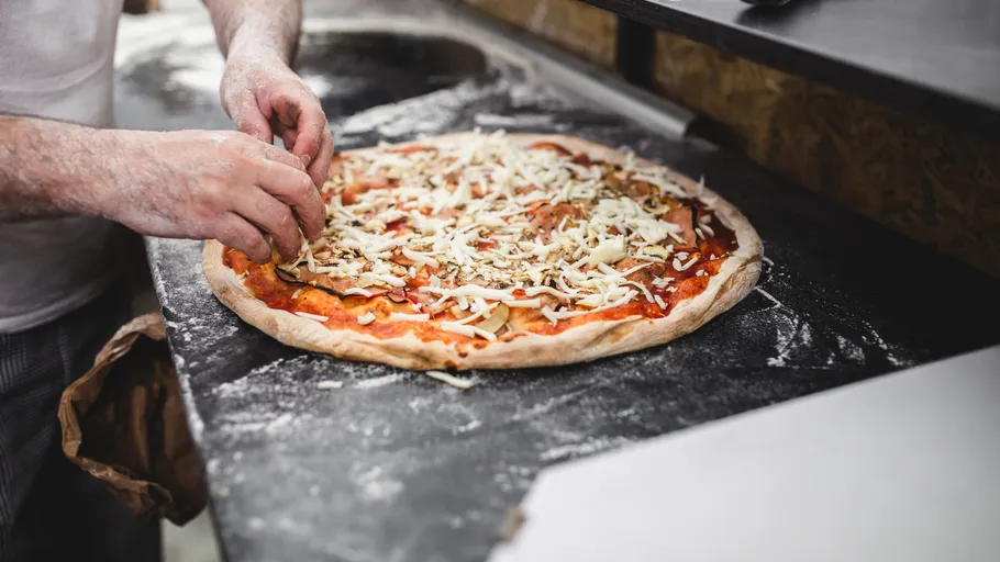 Person fügt Belag zu Pizza in Küche hinzu.