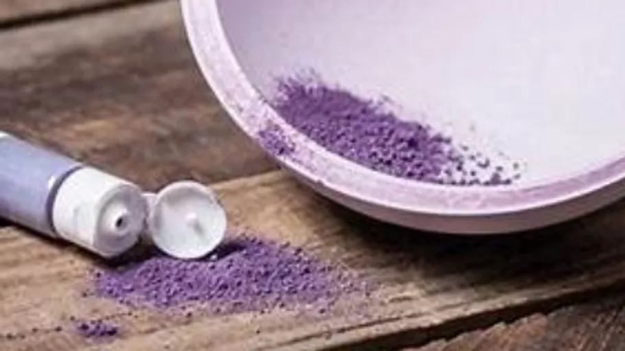 Lila Pulver aus Tube auf Holzfläche verschüttet.