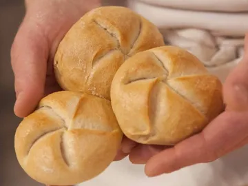 Three rolls are held in hands, freshly baked.