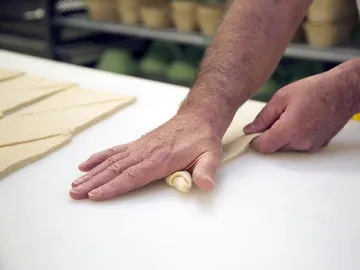 Ein Hand rollt Teig auf einer weißen Oberfläche aus.