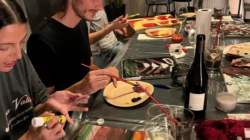 Menschen malen an einem Tisch mit Getränken.