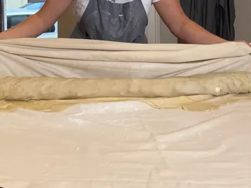 Ein Mensch rollt Teig auf einer Arbeitsfläche aus.