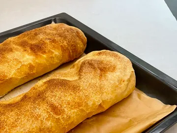 Zwei frisch gebackene Brotlaibe liegen auf einem Blech.
