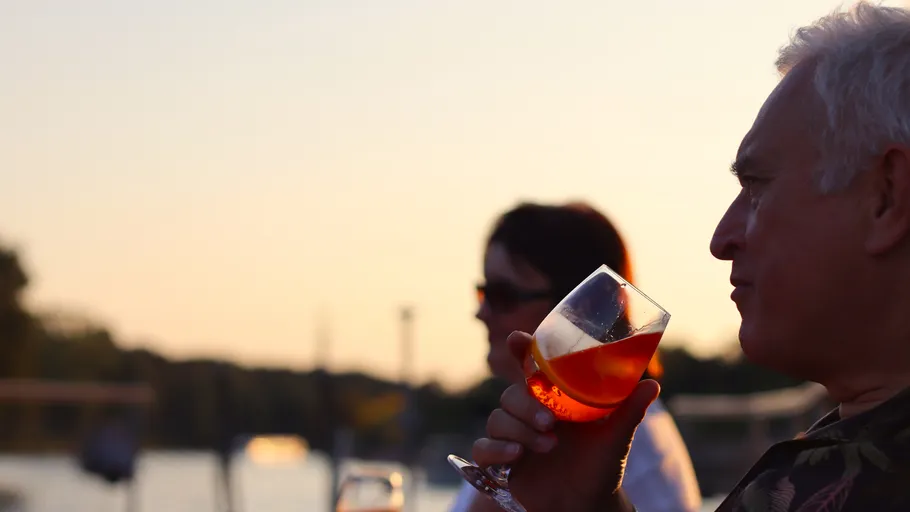 Man drinking wine outdoors at sunset.