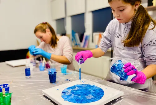 Zwei Mädchen gießen blaue Farbe auf Leinwände drinnen.