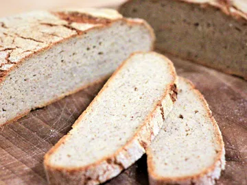 A loaf of bread lies on a wooden board, a few slices.