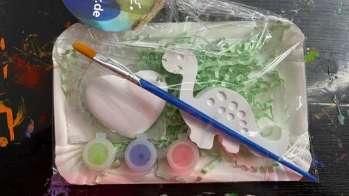 Paintbrush, dinosaur, heart, and paint set on black table.