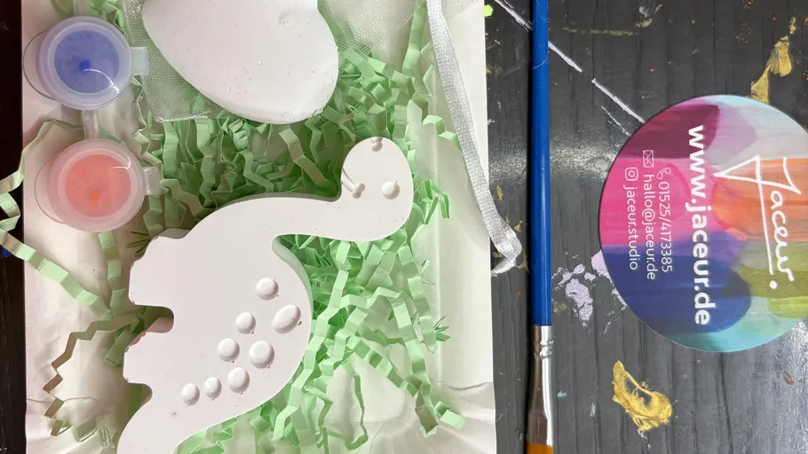 Weiße Dinosaurierfigur mit Farben und Pinsel.