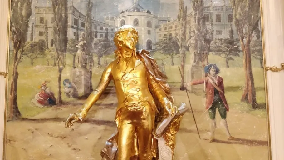 Goldene Statue vor gemaltem landschaftlichem Hintergrund.