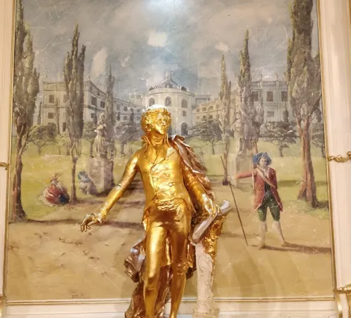 Golden statue of man in front of painting.