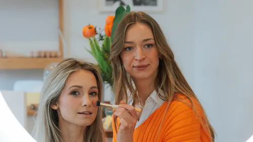 Woman applying makeup to another in bright room.
