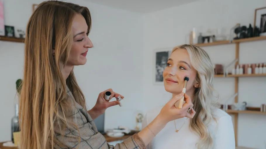 Two women in a room, applying makeup.