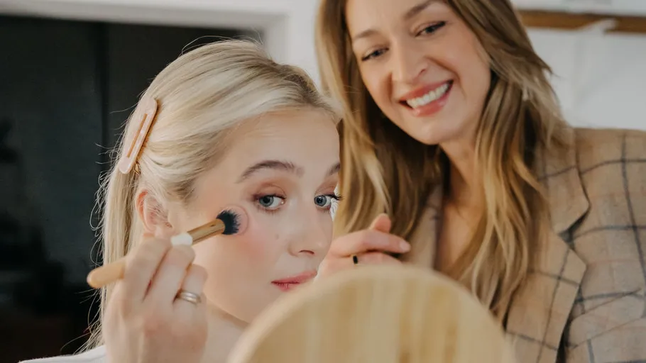 Woman applying blush, another smiling nearby.