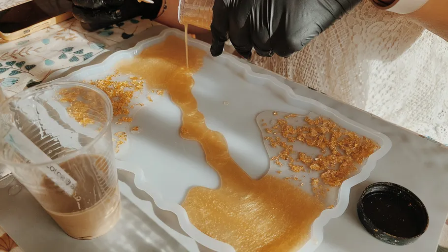 Person pouring resin into mold with gold flakes.