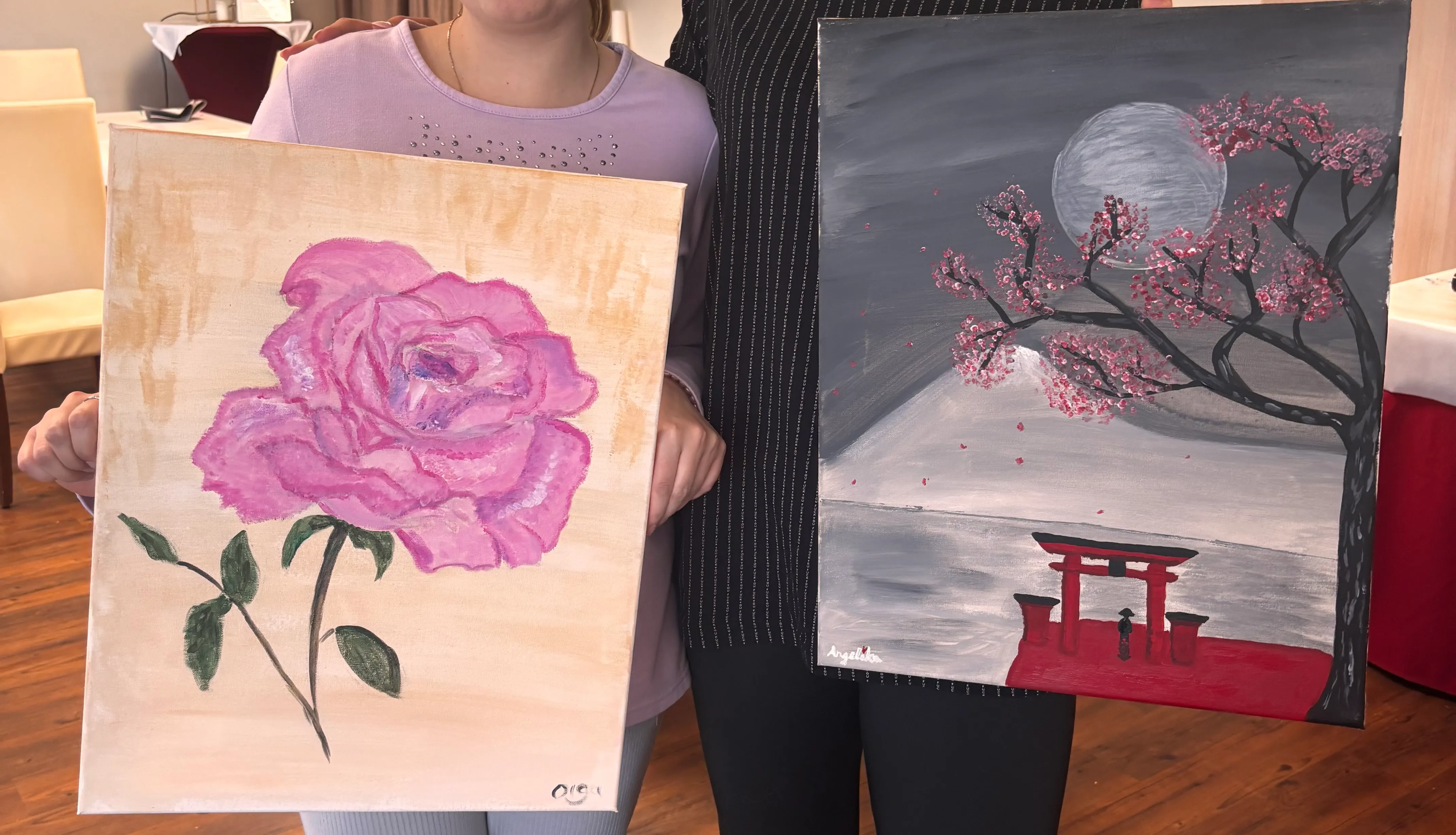 Zwei Personen halten Gemälde, drinnen.