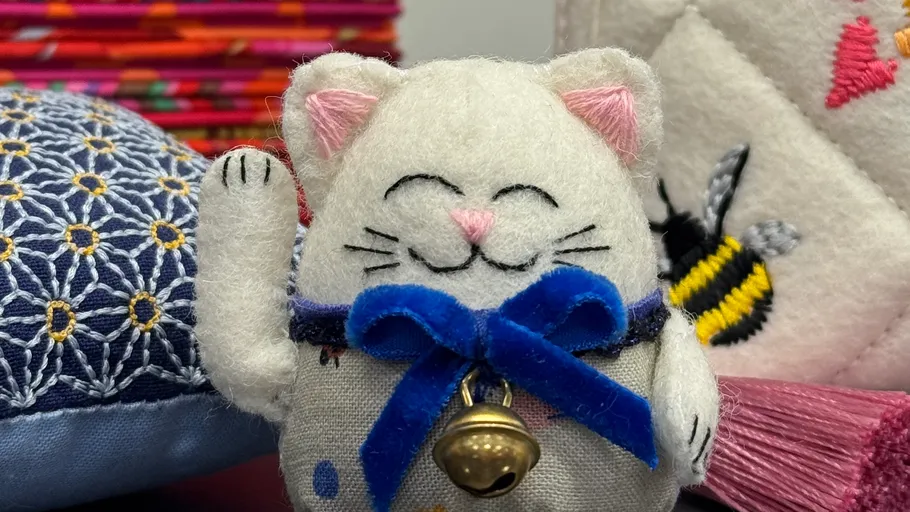 Stoffkatze mit Glocke umgeben von Textilien.