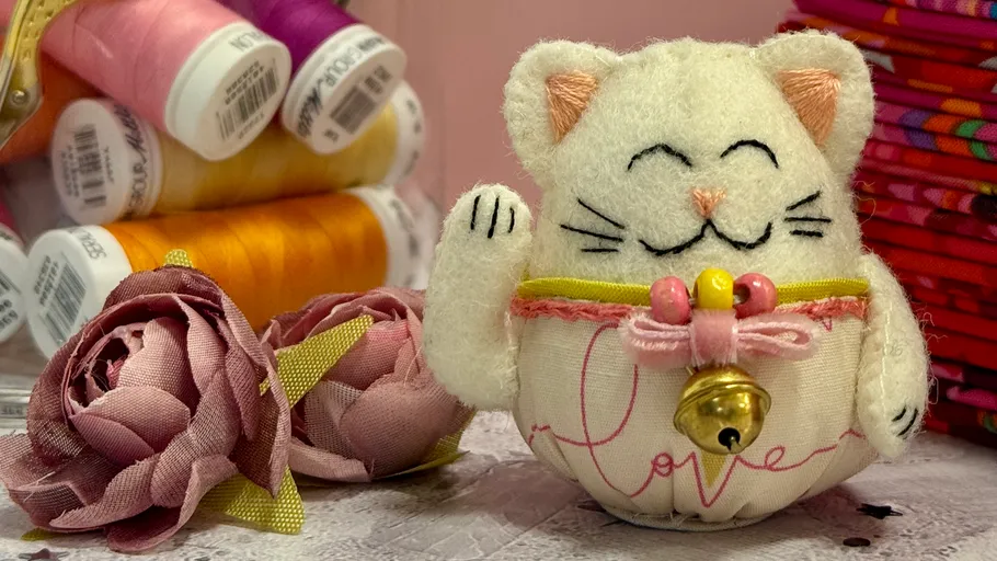 Stoffkatzenfigur neben Garn und Rosen.