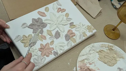 Person painting textured floral design on canvas.