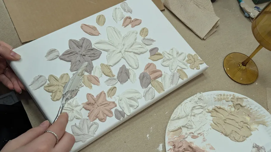 Person malt strukturiertes Blumendesign auf Leinwand.