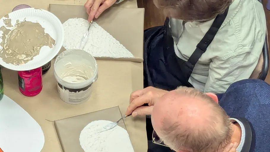 Zwei Personen tragen Gips auf Leinwände auf Tisch auf.